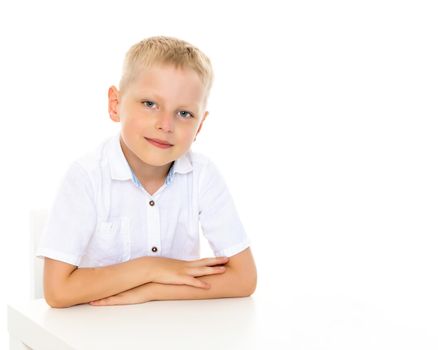 A cute little boy is sitting at a table. The concept of school, child development. Isolated on white background.