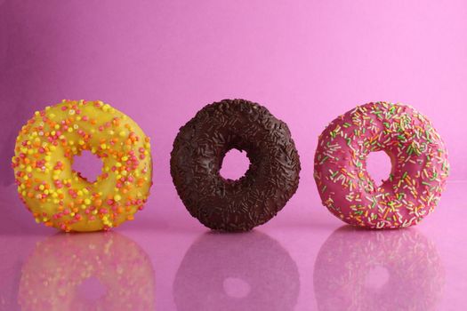 two or three doughnut berliner pink yellow chocolate on a pink background stand falling there is room for text and with a copyspace sweet dessert.