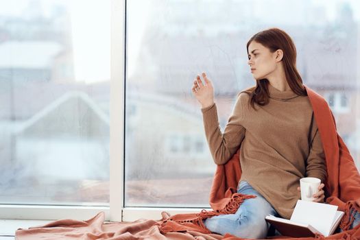 woman with a cup of drink on the windowsill reading a book rest morning. High quality photo