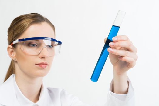 Laboratory analysis and testing. Beautiful woman scientist in protective goggles holding test tube with liquid. Pharmaceutical or chemical industry research and experimentation. Clinic lab examination