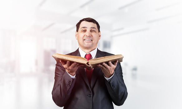 Happy senior businessman holding open book. Portrait of smiling adult man in business suit and tie standing on blurred office background. Education and knowledges. Professional business accounting.
