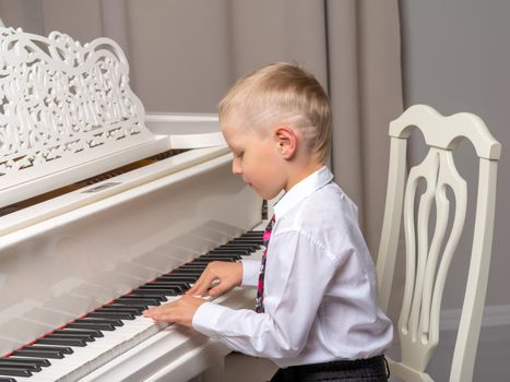 A cute little boy in a studio near a white grand piano. The concept of musical children's education, creative development of the child.