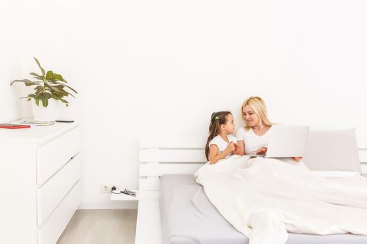 Smiling mother and daughter using laptop in bed at home