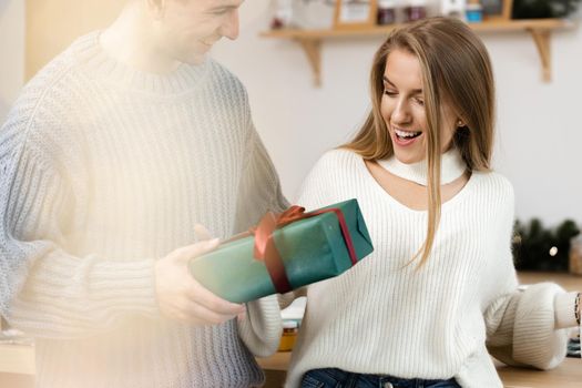 Sweet young couple opening Christmas gifts in the living room at home