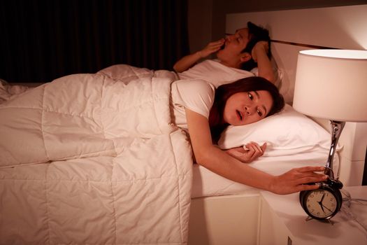 unhappy couple being awakened by an alarm clock in bedroom in the morning
