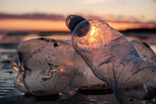 Close-up of plastic bottles thrown on the shore in the backlight. Environmental pollution by plastic. Recyclable packaging.