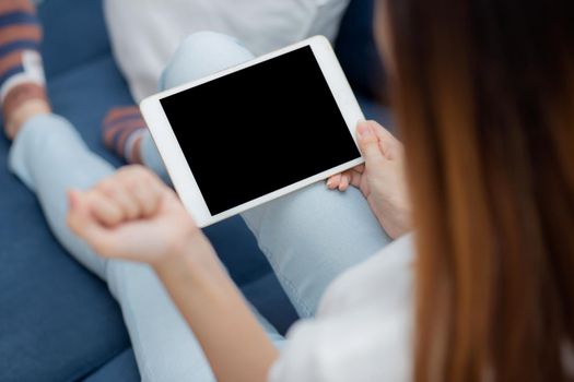 Closeup young asian woman sitting and using mockup of tablet computer with display blank screen on sofa at home, girl holding digital tablet watch entertainment at living room, communication concept.