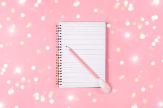 Notepad and pink pen decorated with feather on pink background. Holiday wish list concept.