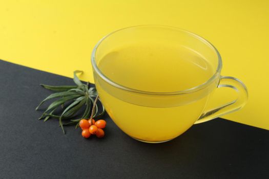 sea buckthorn tea drink on a black yellow bright background. Sea buckthorn drink tea juice in a glass cup next to a spout of sea buckthorn leaves orange berries on a black and yellow background. Creative creative photography. Seasonal berry.