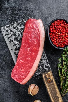 Raw cap rump beef meat steak on a butcher cleaver. Black background. Top view.