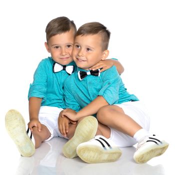 Two cute little boys, brothers sit on the floor in a studio on a white background. The concept of a happy childhood, the development of a child in the family. Isolated.