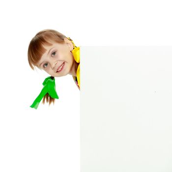 A beautiful Caucasian little blonde girl with long pigtails, in which large colored bows are braided, and a short bangs on her head. In a short summer dress.Looks because of the white obstacle.