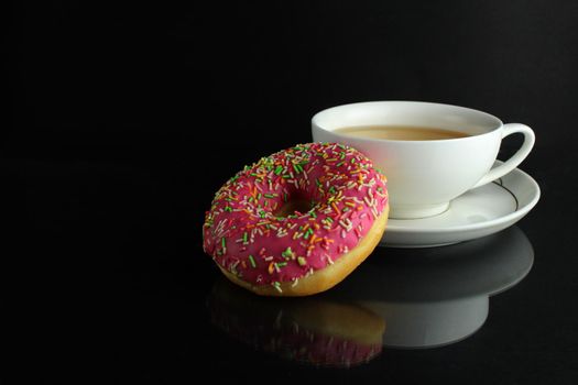 Doughnut with pink icing berliner lies next to a cup of coffee tea delicious breakfast snack day without diet on black background copyspace.