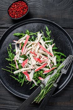 Crab meat on a plate with arugula. Black background. Top view.