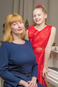 A beautiful young mother with a little daughter near a large white grand piano. The concept of family happiness, music education.