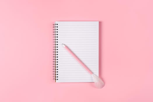 Notepad and pink pen decorated with feather on pink background. Woman power concept.