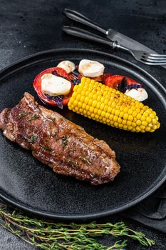 Roasted P beef steaks Striploin or New York on a plate with garnish. Black background. Top view.