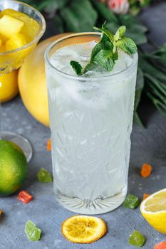 Summer fresh cold drink beverages. Ice Lemonade in the jug and lemons and orange with mint on the table outdoor. Orange lemonade in a glass.