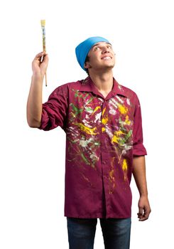 Smiling young painter artist holding paintbrush. Portrait of happy painter looking upwards isolated on white background. Creative hobby and artistic occupation. Art school student posing.