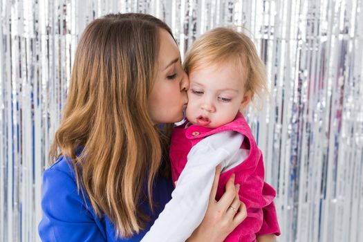 Childhood, holidays and family concept - Mother kissing baby daughter on shiny background. Close-up.