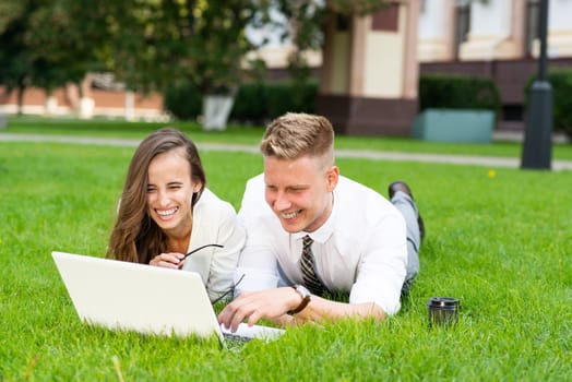 man and woman work with a laptop on grass in park. Business-building concept