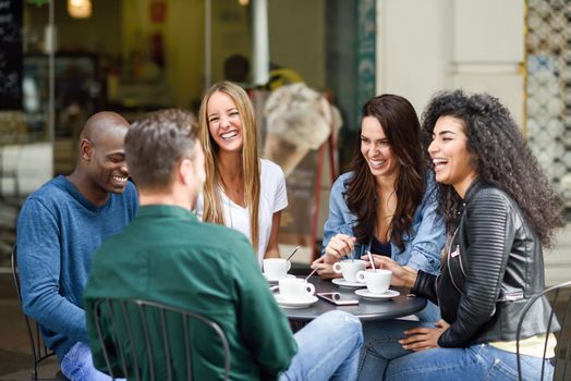 Multiracial group of five friends having a coffee together. Three women and two men at cafe, talking, laughing and enjoying their time. Lifestyle and friendship concepts with real people models