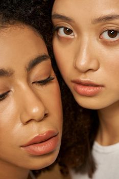 Face closeup of two beautiful mixed race young women with perfect glowing skin posing together. Skincare, diversity concept. Selective focus. Vertical shot