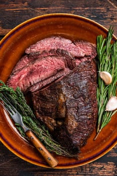 Roasted hanger or Onglet sliced beef meat steak on a rustic plate with cleaver. Dark wooden background. Top View.