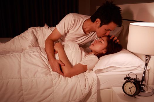 young man kissing his wife in bed at night