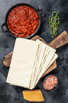 Raw Different ingredients for cooking Italian lasagna on a kitchen table. Black background. Top view.