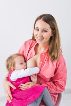 Lactation and motherhood concept - Young beautiful mother holding breastfeeding baby sitting on chair