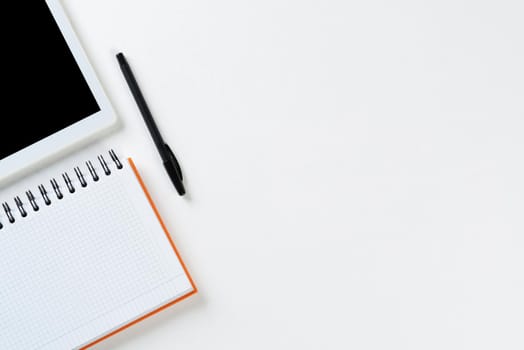 Top view of modern working place. Spiral notepad, pen and tablet computer on white surface. Education, creativity and innovation concept with copy space. Digital technology in modern business.