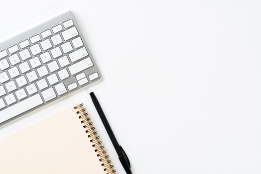 Top view of modern working place. Spiral notepad, pen and computer keyboard on white surface. Education, creativity and innovation concept with copy space. Digital technology in modern business.