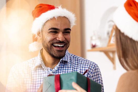 Romantic multiethnic couple in Christmas hats exchanging gifts, close up portrait