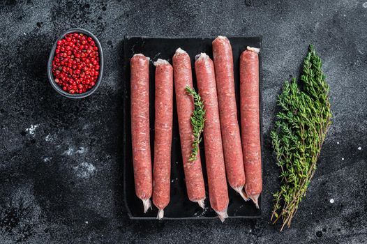 Fresh Raw butchers sausages in skins with thyme on marble board. Black background. Top view.