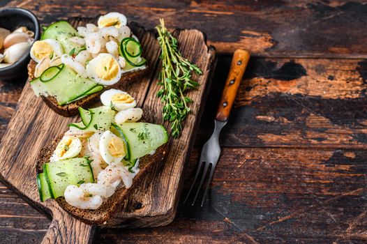 Sandwiches with shrimp, prawns, quail eggs and cucumber on rye bread. Dark Wooden background. top view. Copy space.