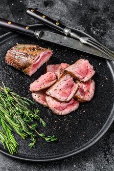 BBQ grilled and Sliced veal tenderloin meat steak on a plate. Black background. Top view.