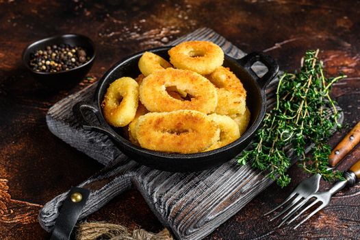 Fried squid rings breaded on a cutting board. Dark background. Top view.