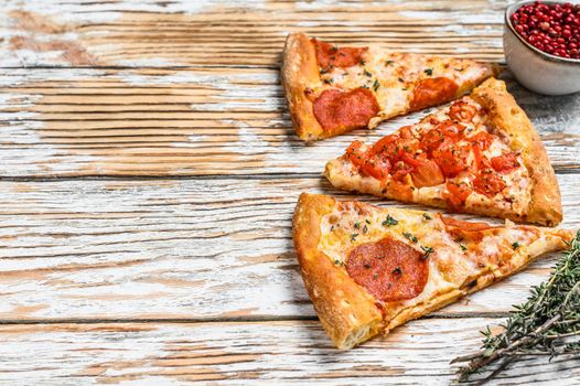 Pieces of pepperoni and tomato pizza. White wooden background. Top view. Copy space.