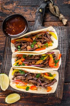 Tacos shells with pork meat, onion, tomato, sweet pepper and salsa. Mexican food. Dark wooden background. Top view.