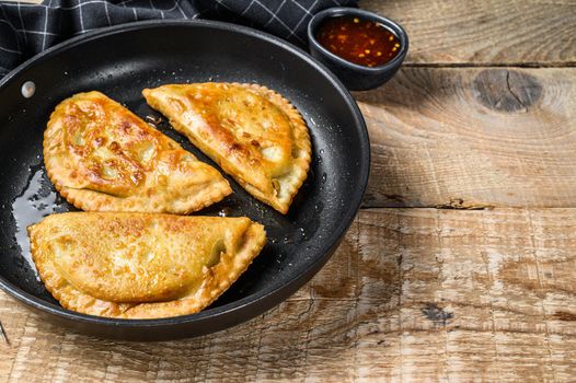 Fried empanadas savoury pastries with beef meat stuffing in a pan. Wooden background. Top view. Copy space.