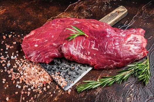 Flap or Flank raw beef meat steak on a butcher cleaver with herbs. Dark background. Top view.