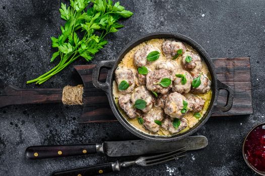 Beef meatballs in cream sauce in a frying pan. Black background. Top view.