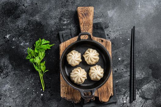 Dim sum stuffed meat dumplings in a pan with herbs. Black background. Top view.