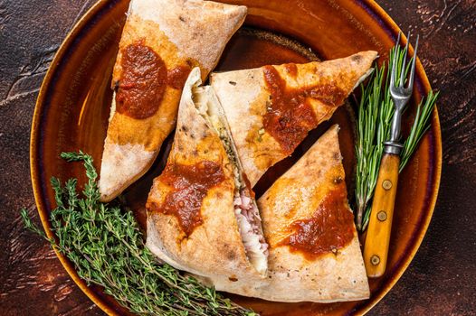 Calzone pizza pieces on rustic plate with tomato sauce and herbs. Dark background. Top view.