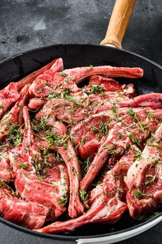 Raw fresh lamb rib chops marinated with thyme and mint in a pan. Black background. Top view.