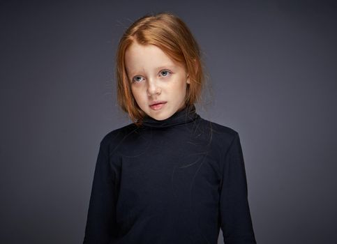 red-haired girl with freckles on her face in a black sweater posing. High quality photo