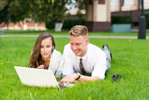 man and woman work with a laptop on grass in park. Business-building concept