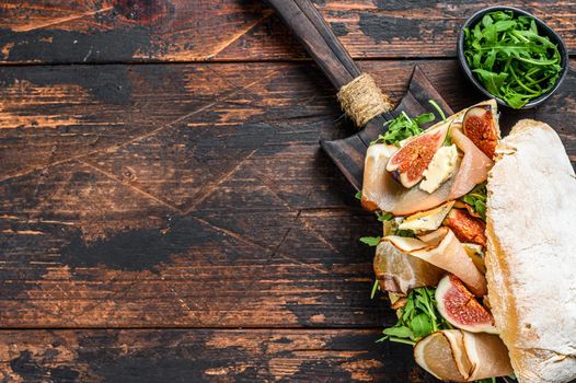 Ciabatta sandwich with romaine salad, prosciutto and mozzarella cheese. Dark Wooden background. Top view. Copy space.