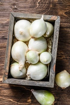 White raw onion in wooden box. Wooden background. Top view.